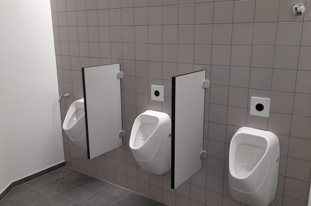 Sanitäranlage mit Urinalen und Trennwänden Sanitärbereich mit drei weißen Urinalen an einer grau gefliesten Wand