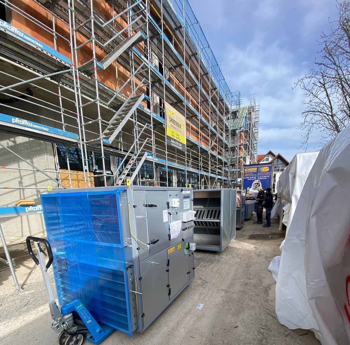 Baustelle mit Gerüst und Lüftungsgeräten im Vordergrund. Foto einer Großbaustelle mit Sanitärenanlagen vor dem Gerüst des Hauses